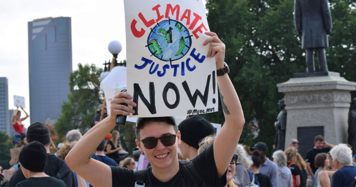 Move Minnesota staff, Finn McGarrity, holding sign "We want climate justice now!" at Youth Climate Strike