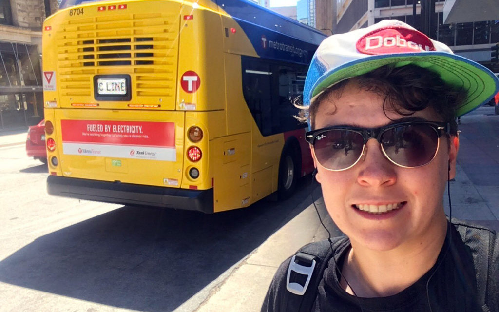 Move Minnesota community organizer Finn McGarrity takes a selfie next to a new C Line bus that says "Fueled by Electricity" on the back.