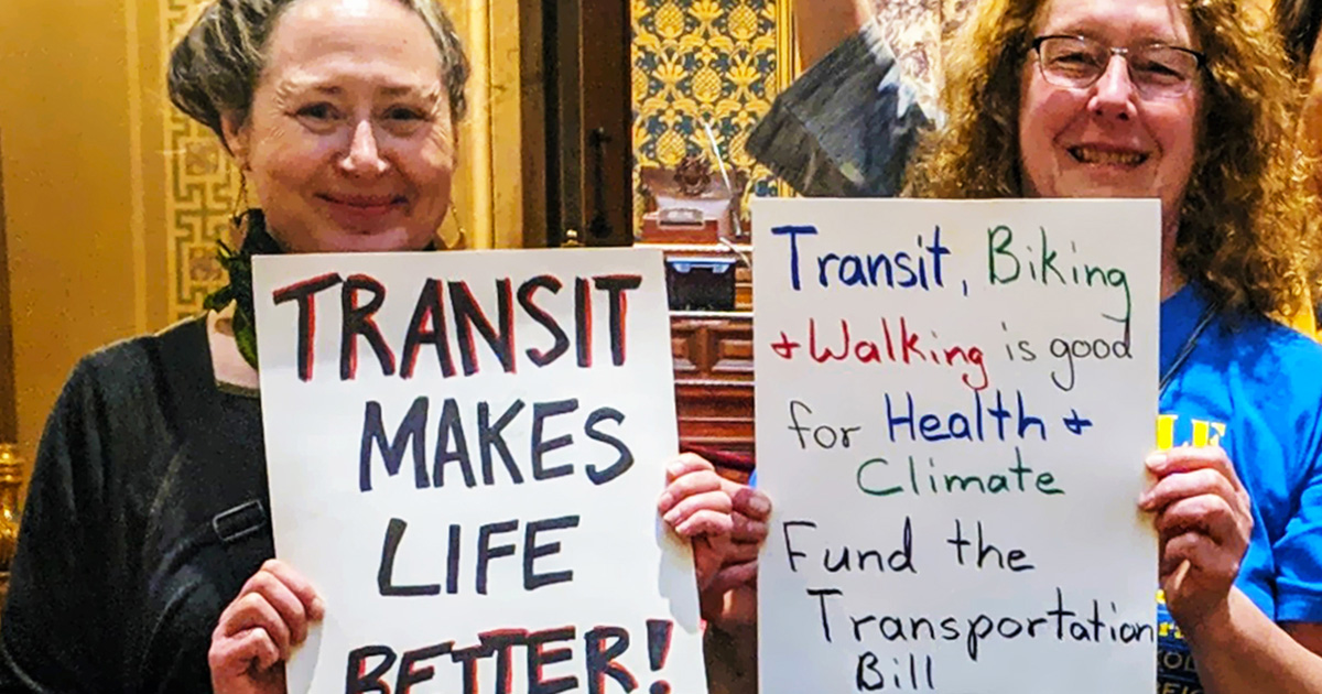 Advocates hold signs with pro-transit messages. One sign says, "Transit Makes Life Better."