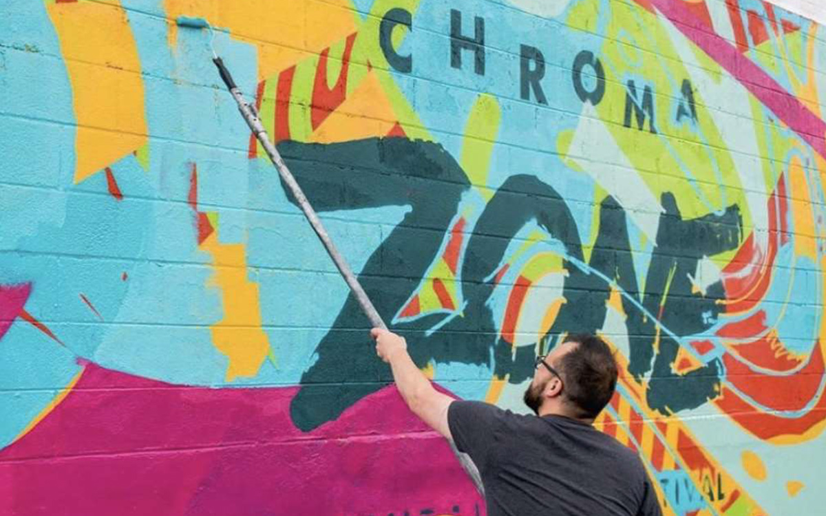 An artist paints a colorful Chroma Zone mural for the festival in Saint Paul.