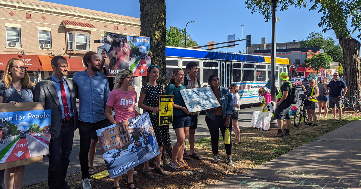 Bus lane and bike lane supporters gathered for an outdoor action along Hennepin Ave S in Minneapolis. A Metro Transit bus passes in the background.