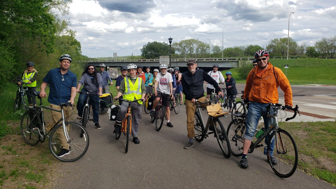 A group of people on a Move Minnesota bike ride gather with their bikes on a paved trail in Saint Paul.