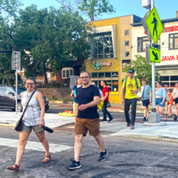 Two smiling people crossing Lyndale Avenue in a crosswalk with a line of pedestrians behind them