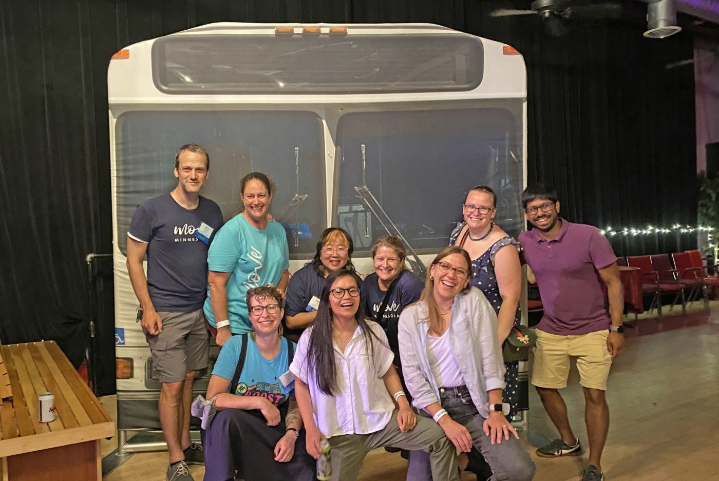 The Move Minnesota staff smiling and posing in front of a life-sized banner of a Metro Transit bus