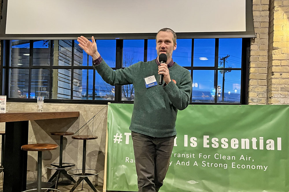 Move Minnesota Executive Director Sam Rockwell, a white man with a beard wearing a green sweater, outlined Move Minnesota's policy priorities for the 2024 legislative session