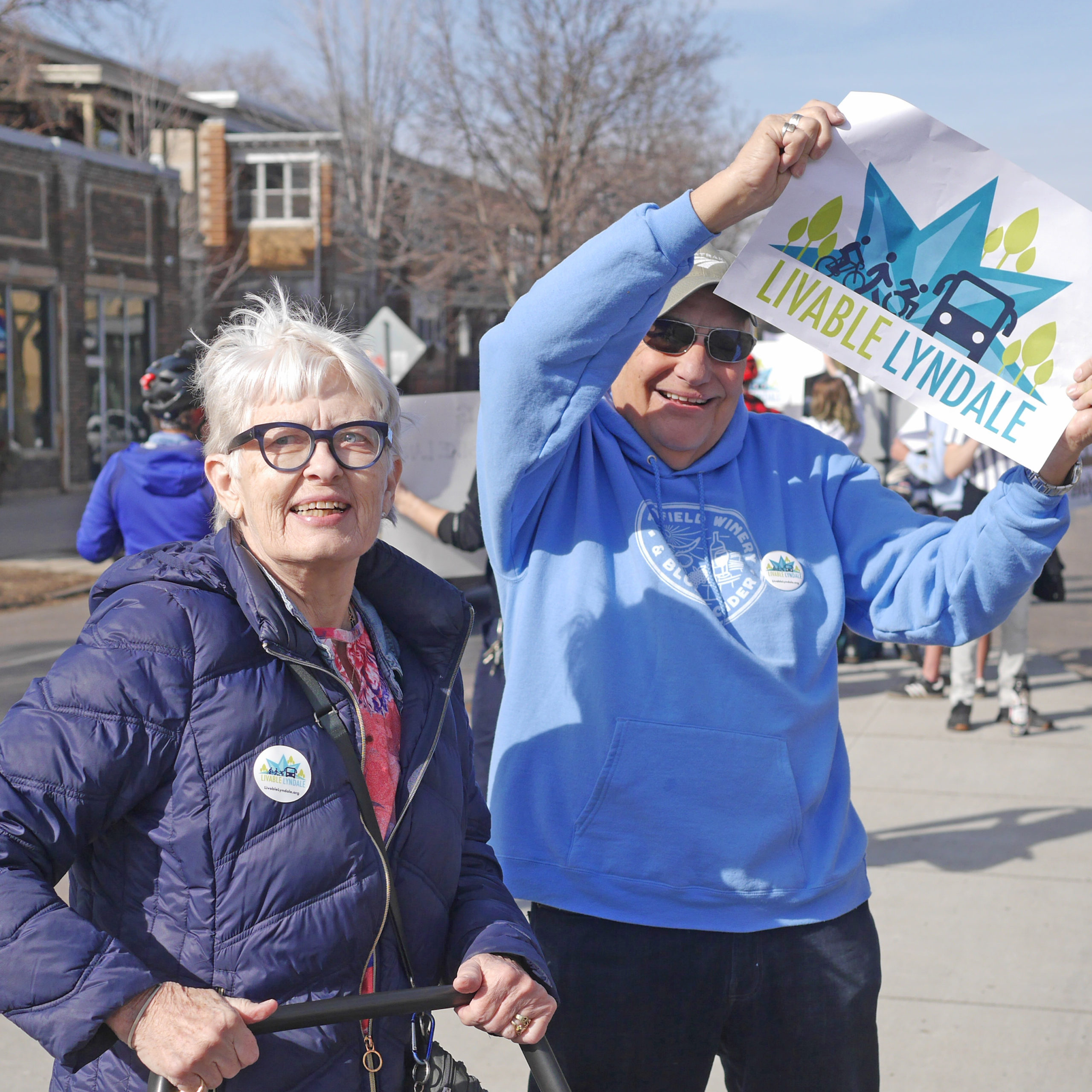 Two elder community members wearing Livable Lyndale buttons and holding a Livable Lyndale sign at the rally in Minneapolis.
