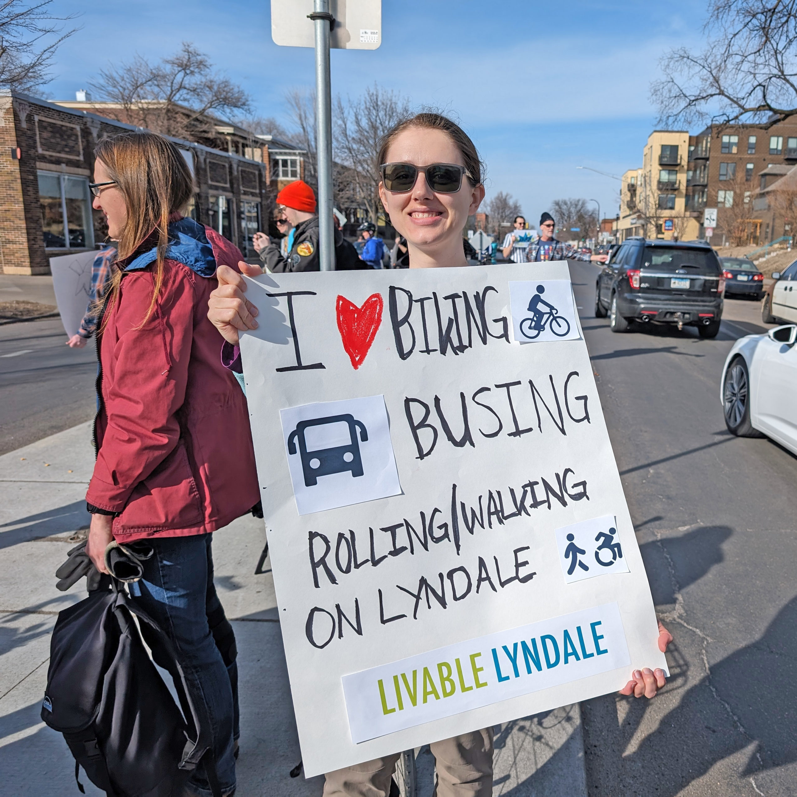A community member at the Livable Lyndale rally in Minneapolis holds a hand-made sign that says "I love biking, bus, rolling/walking, on Lyndale."