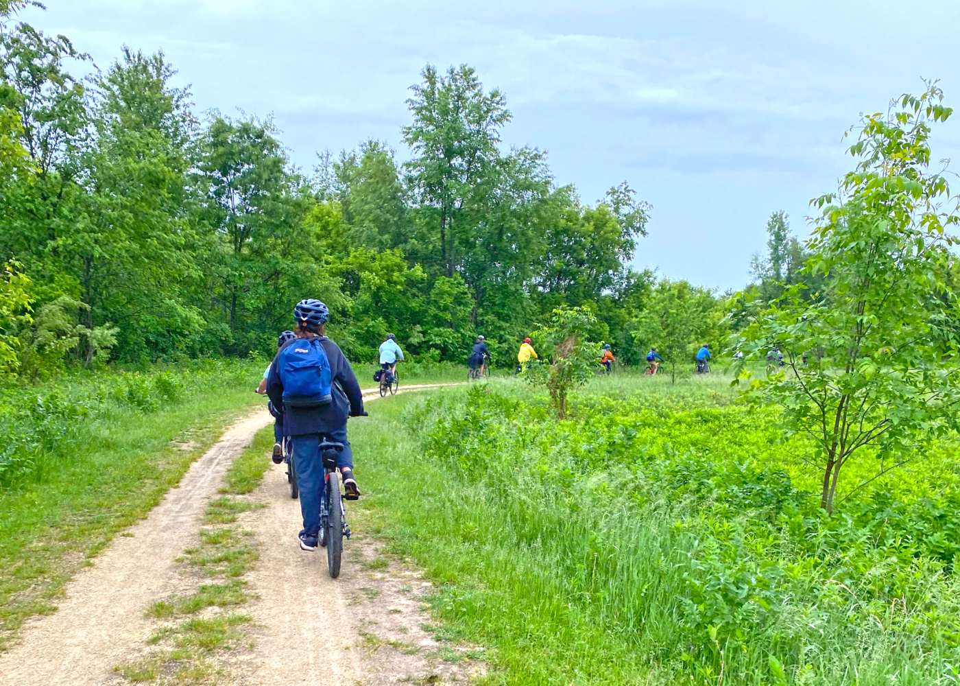 A group of students bicycling on a dirt path through a lush green meadow