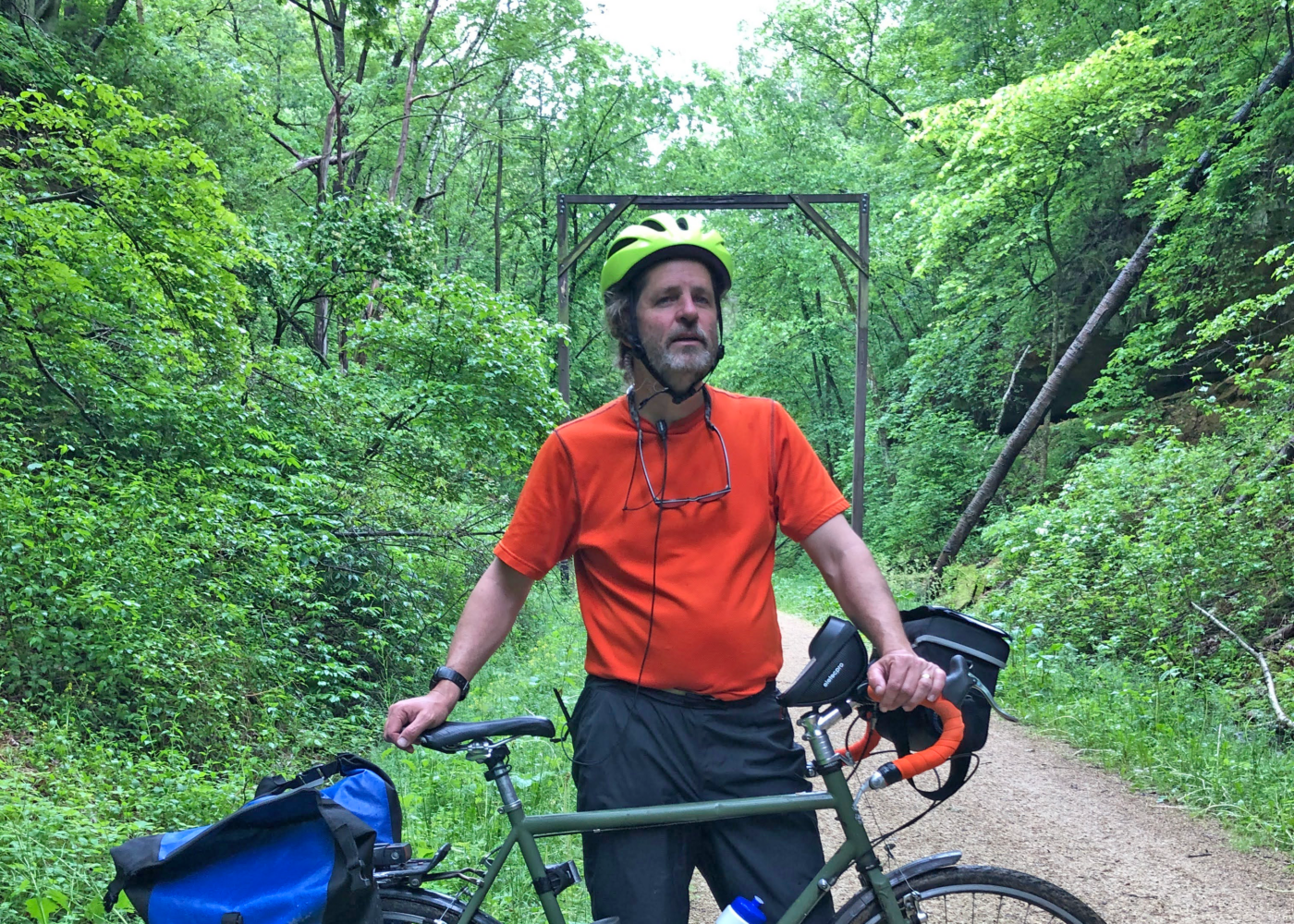 Photo of Nick Beerman, a white man with a gray beard, wearing a bright yellow bike helmet and standing behind his bicycle