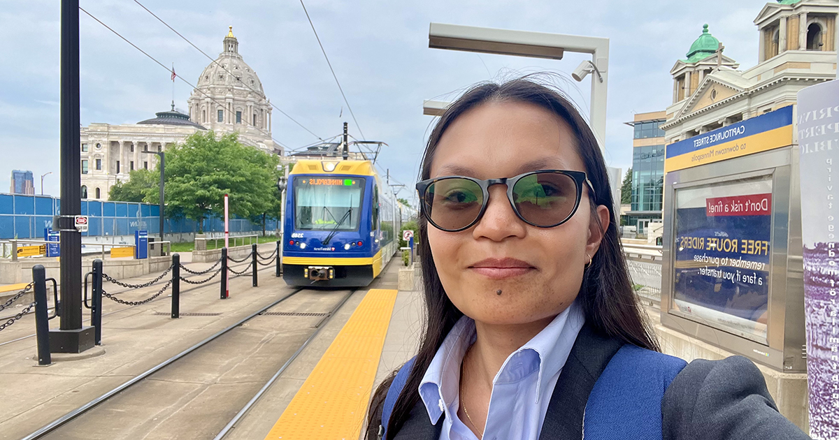 MJ Carpio at a Green Line Station in Saint Paul. A light rail train and the Minnesota State Capitol building are both visible in the background.