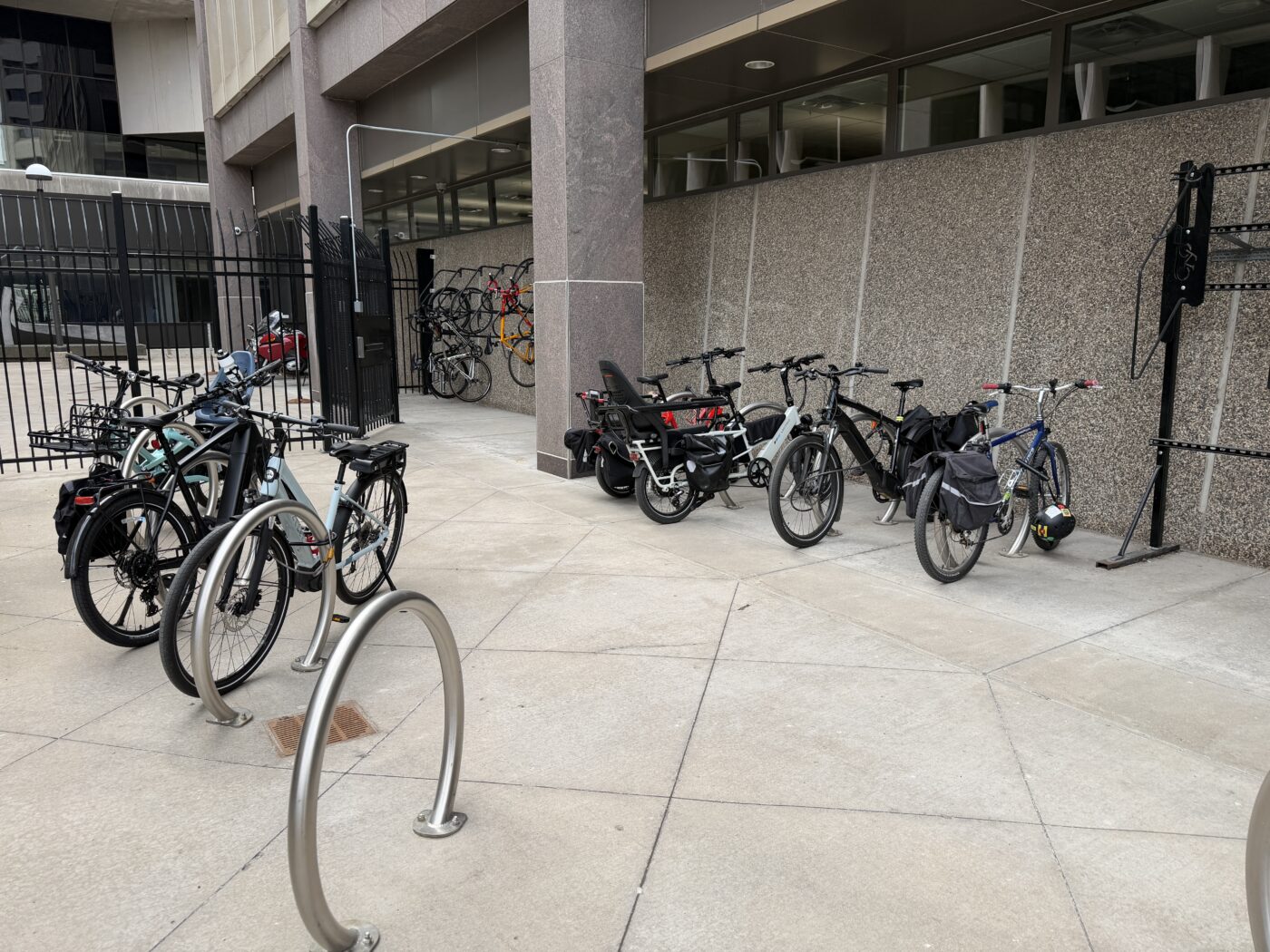 A gated bike locking area outside the Metropolitan Council building with over 10 bikes on various hanging and ground storage spots.
