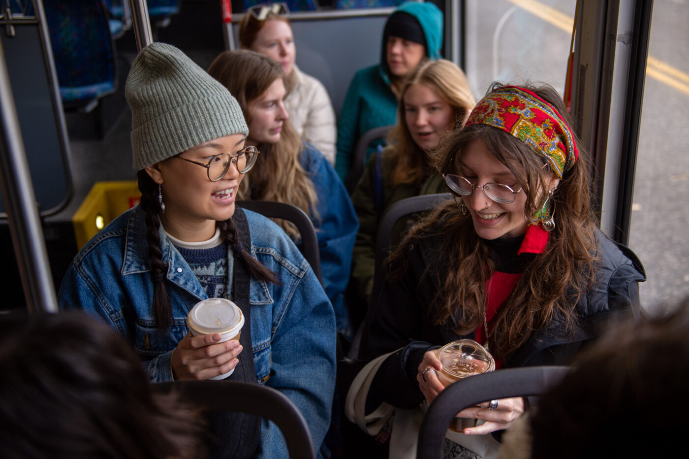 Two young people sit together and smile while chatting and riding the bus.